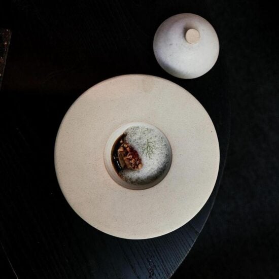 A white ceramic plate with a central depression for serving food, displayed alongside a smaller cloche functioning as a lid.