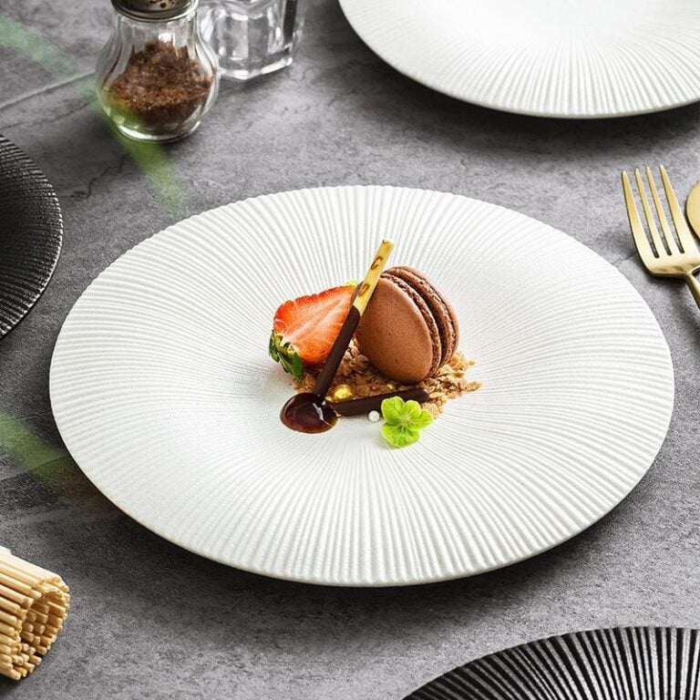 A white ceramic plate with a ridged edge design, displaying a plated dessert consisting of a chocolate mousse, strawberry, and a macaroon.