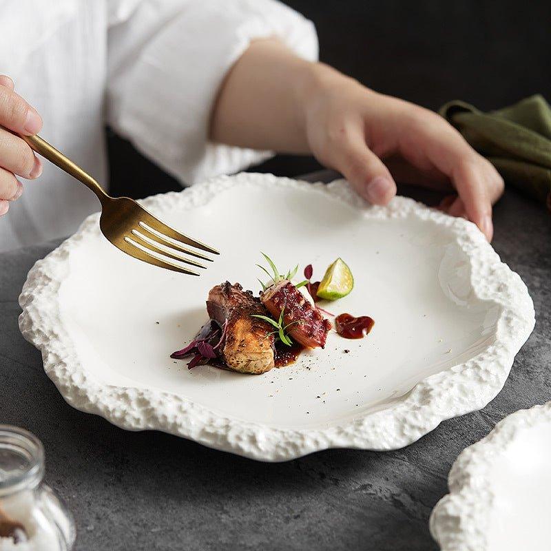 Assiette plate en céramique blanche à bord irrégulier et texturé, évoquant la pierre.