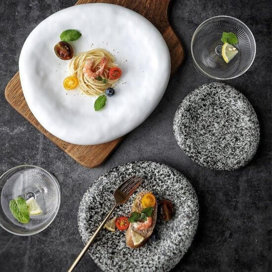 A set of dinner plates with one plate having food presented on it, placed on a wooden board, with the rest of the plates showing a textured grey surface.
