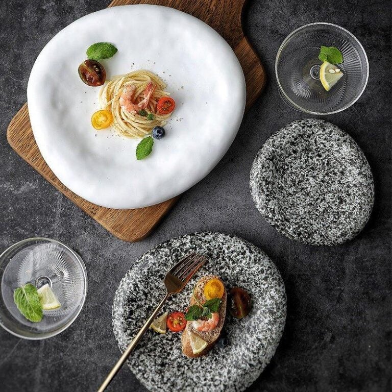 A set of dinner plates with one plate having food presented on it, placed on a wooden board, with the rest of the plates showing a textured grey surface.