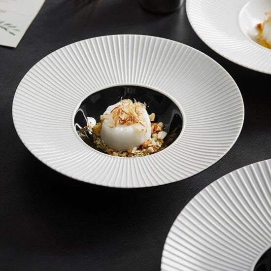 A white plate with a central depression, resembling a hat, filled with food, placed on a black surface.